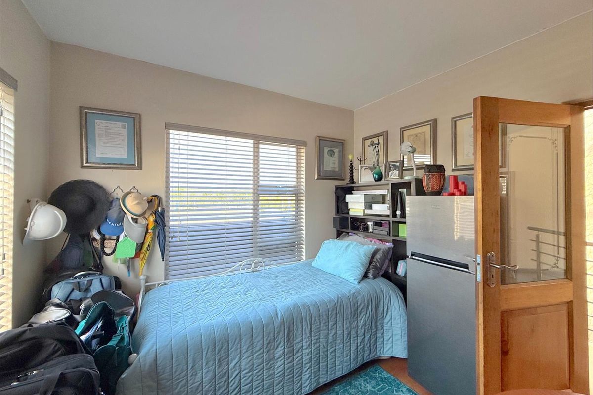 A functional bedroom featuring a window with fitted blinds and a wooden door with glass paneling.