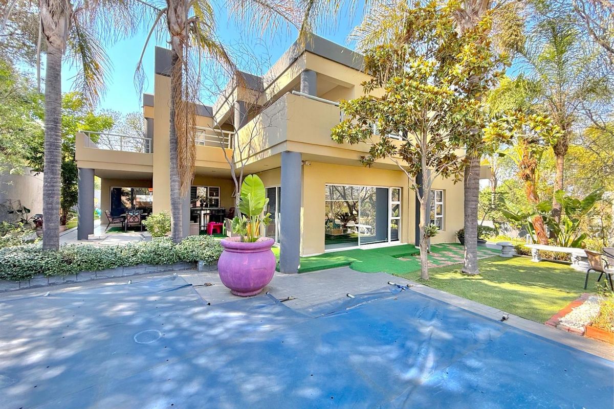 A rear view of a multi-story residential property featuring a covered patio, balcony, and a swimming pool with a safety cover.