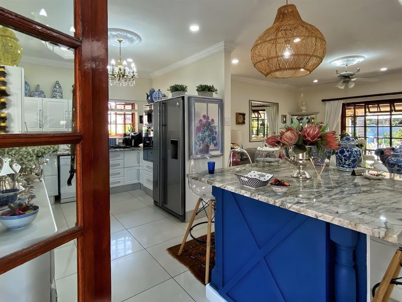 A bright open-plan kitchen featuring a central island with stone countertops, white cabinetry, and tiled flooring, seamlessly connecting to the living area.