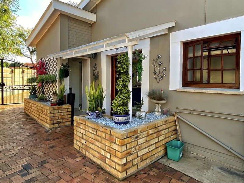 Front entrance area featuring brick planter boxes, a timber pergola, and paved driveway access with secure gated entry.