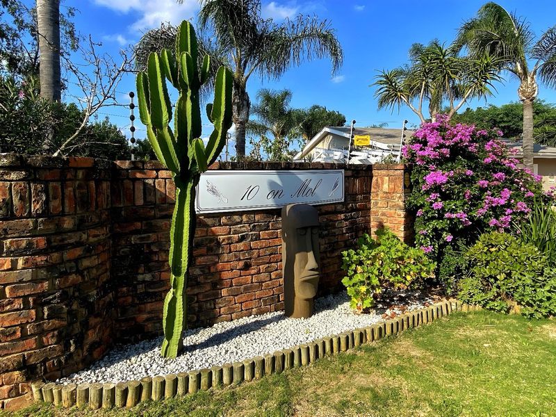 Front boundary wall featuring brick masonry, electric security fencing, and established garden landscaping with a decorative property sign.