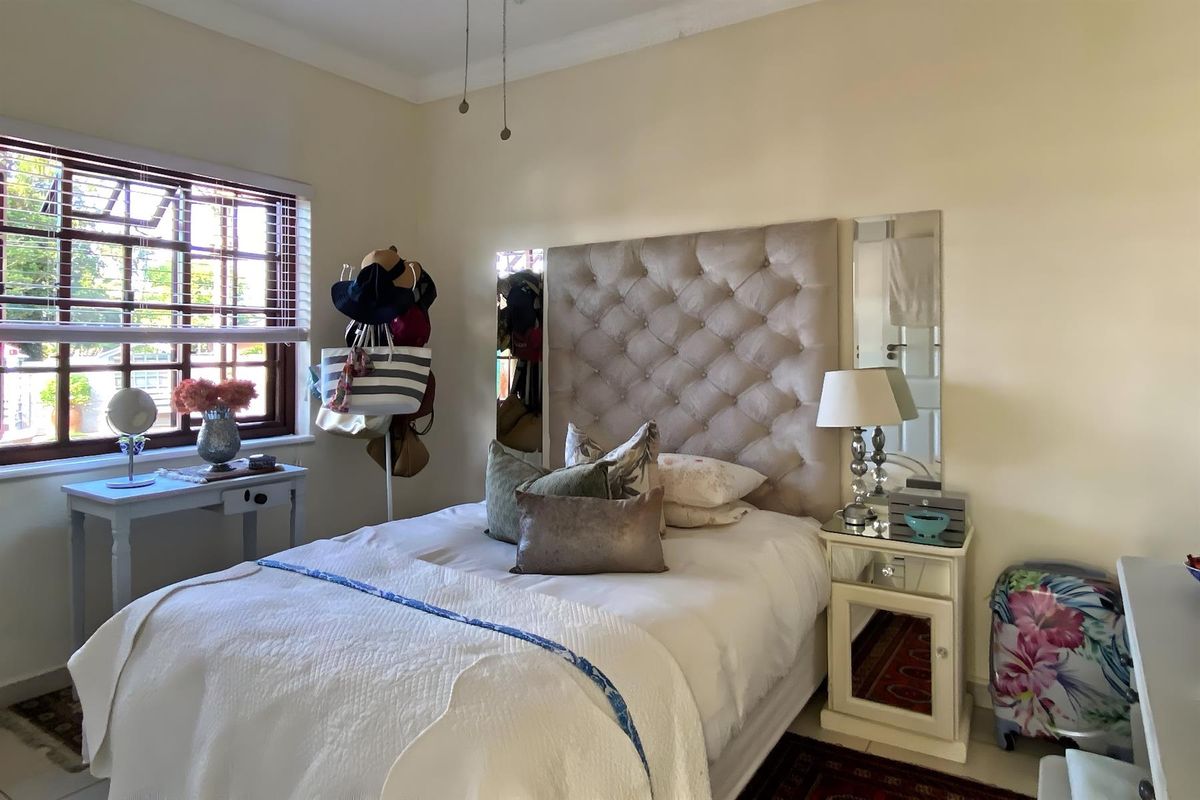 A cozy bedroom featuring a tufted headboard, timber-framed windows with venetian blinds, and a ceiling fan.
