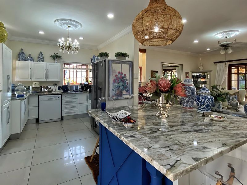 Spacious open-plan kitchen featuring a large central island with stone countertops, ample built-in cabinetry, and modern tiled flooring, seamlessly flowing into the living area.