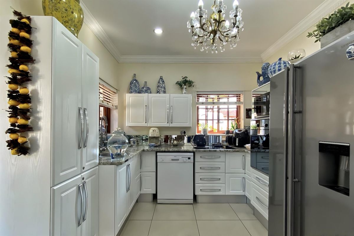 A well-maintained kitchen featuring white cabinetry, granite countertops, tiled flooring, and a classic chandelier, offering a bright and functional culinary space.