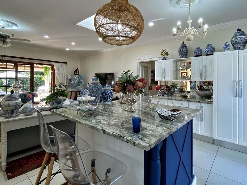 Spacious open-plan kitchen and living area featuring a large stone-topped island, modern cabinetry, skylight, and seamless flow to the outdoor patio.