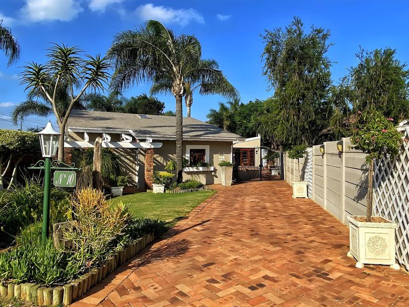 A well-maintained front exterior featuring a brick-paved driveway, landscaped garden, pergola, and secure gated entrance.