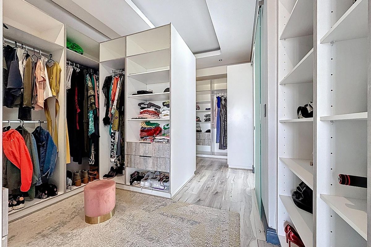 A modern walk-in closet featuring extensive built-in white cabinetry, recessed ceiling lighting, and durable laminate flooring.