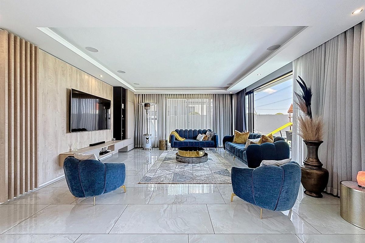 Spacious modern living room featuring large format floor tiles, a custom built-in media wall, and expansive sliding glass doors leading to the outdoor area.