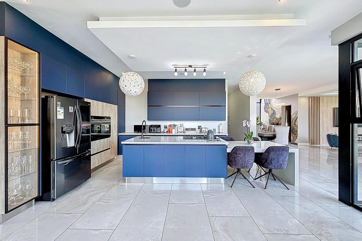 Modern open-plan kitchen featuring navy blue cabinetry, a central island with stone countertops, integrated appliances, and high-end porcelain floor tiles.