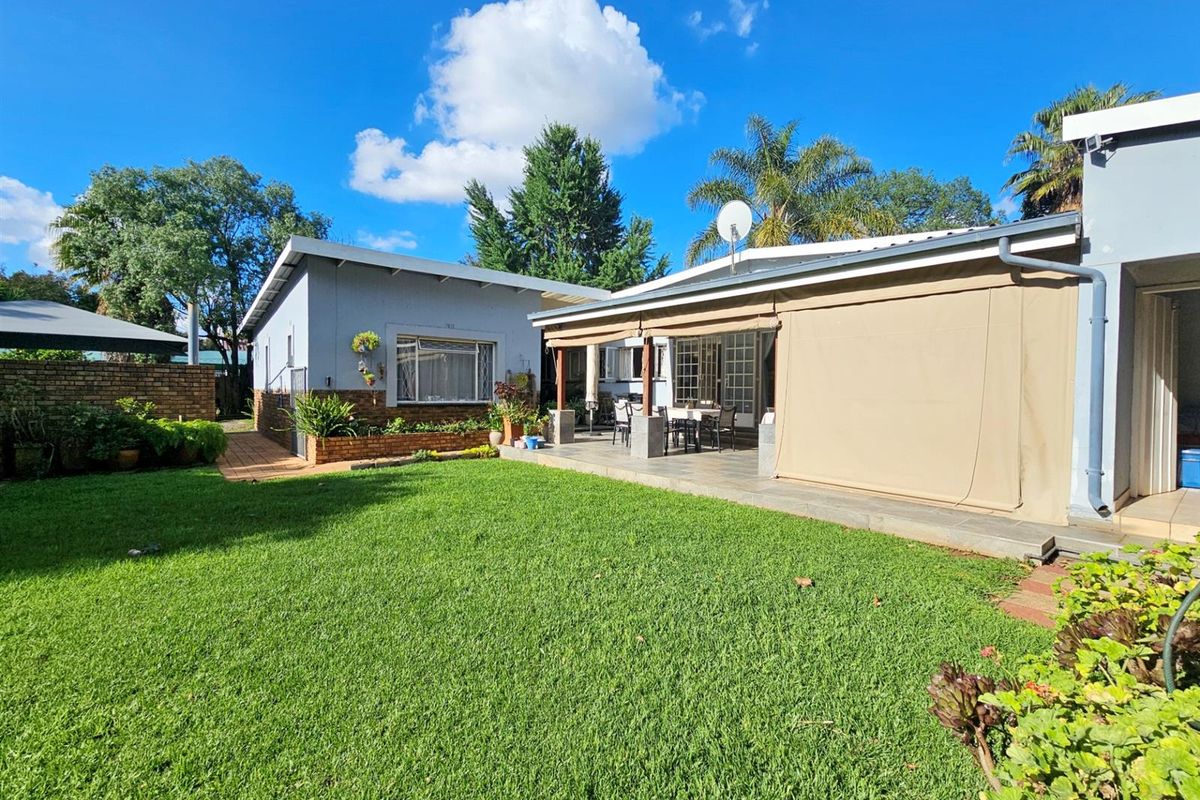 A well-maintained rear garden featuring a spacious paved patio area with retractable outdoor blinds, overlooking a neat lawn and established landscaping.