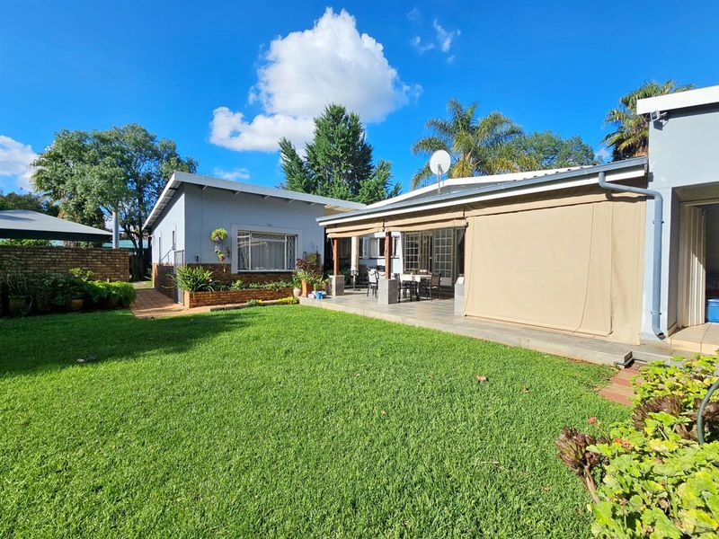 A well-maintained rear garden featuring a spacious paved patio area with retractable outdoor blinds, overlooking a neat lawn and established landscaping.