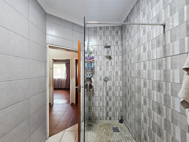 A modern bathroom featuring a walk-in shower with a glass screen, contemporary grey wall tiling, and a rainfall showerhead.