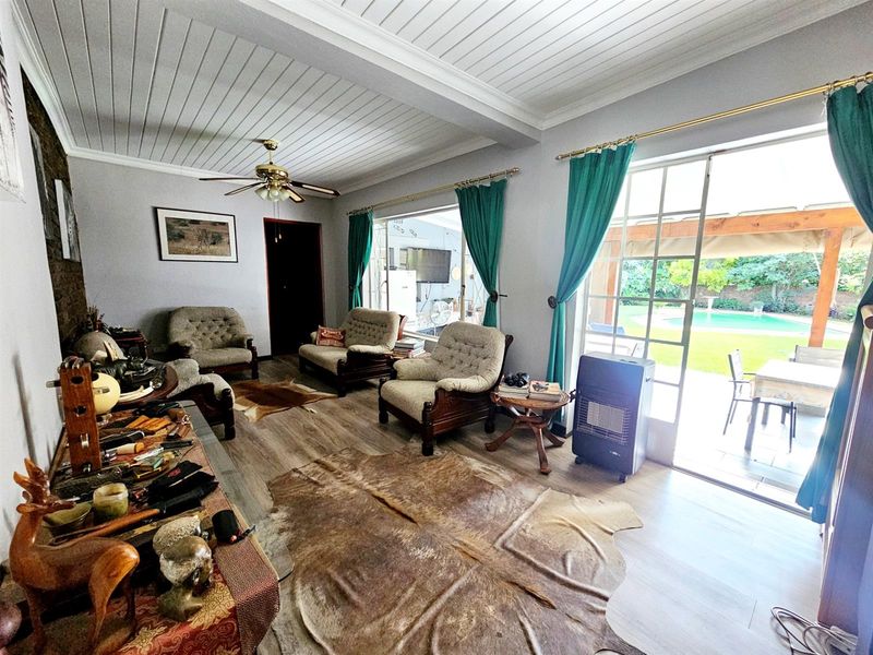 Spacious living room featuring wood-look flooring, a tongue-and-groove ceiling, and large glass doors providing direct access to the outdoor patio and pool area.