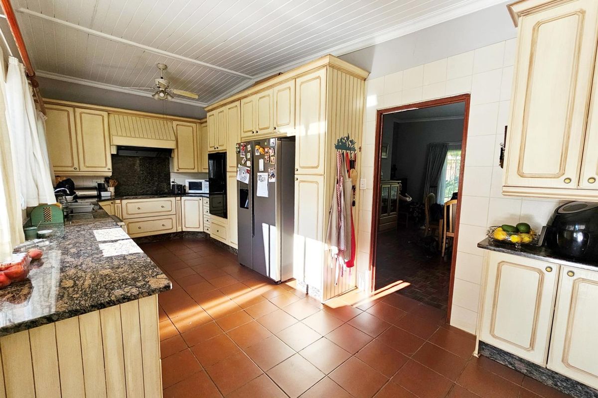 Spacious kitchen featuring cream-toned cabinetry, granite countertops, tiled flooring, and a built-in oven, offering a functional layout with direct access to the living area.
