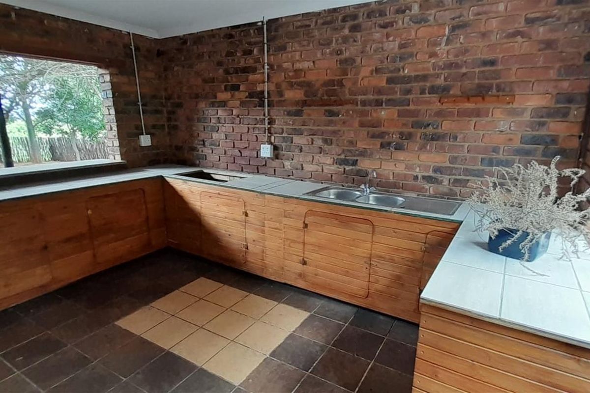 A rustic kitchen area featuring exposed brick walls, wooden cabinetry, and a double-basin sink, offering a functional space with potential for modernization.