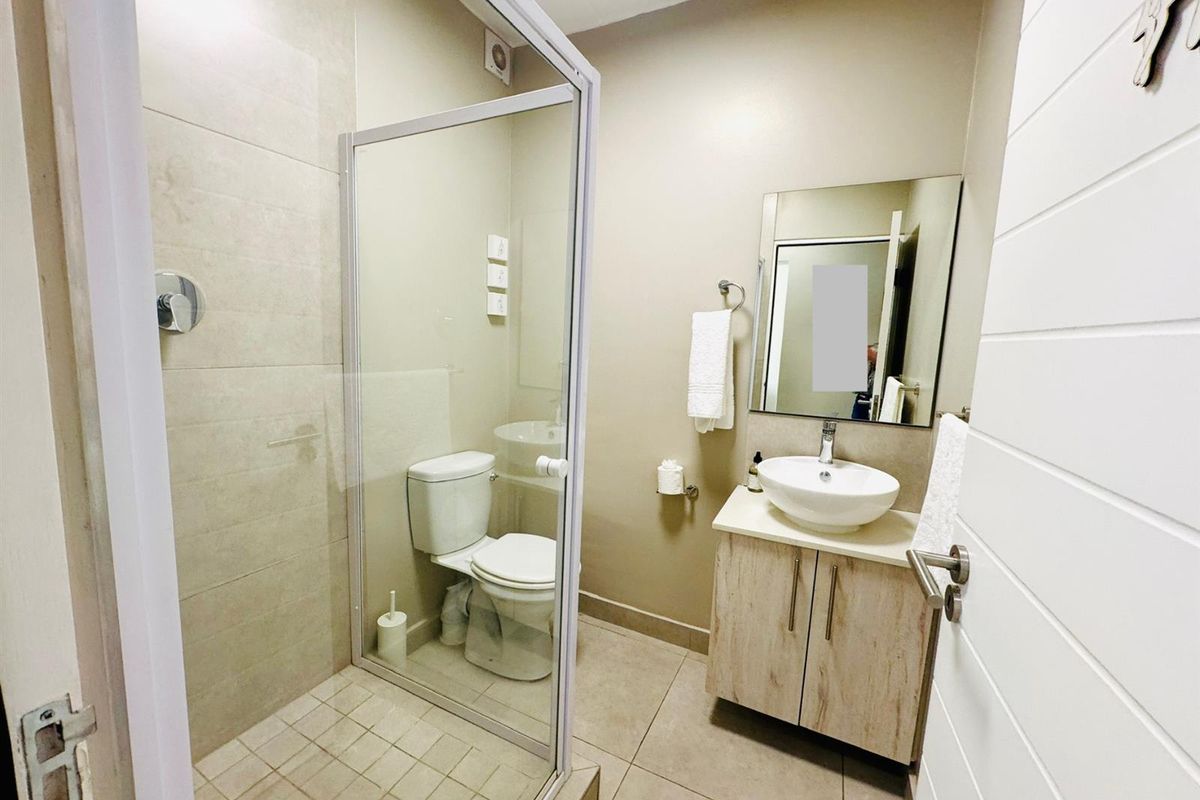 A modern bathroom featuring a glass-enclosed shower, a vessel sink vanity with wood-look cabinetry, and neutral floor-to-ceiling tiling.