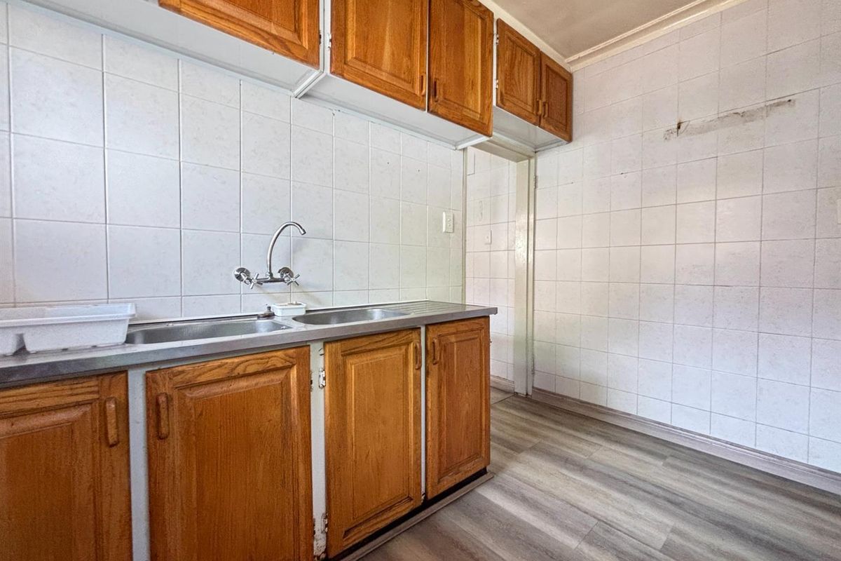 A dated kitchen area featuring wooden cabinetry, a stainless steel sink, and tiled walls, offering a blank canvas for renovation.