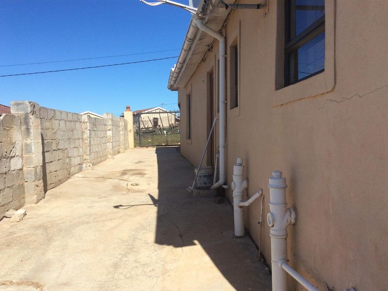 Rear exterior view of the property featuring a concrete paved side path, boundary wall, and exposed external plumbing infrastructure.