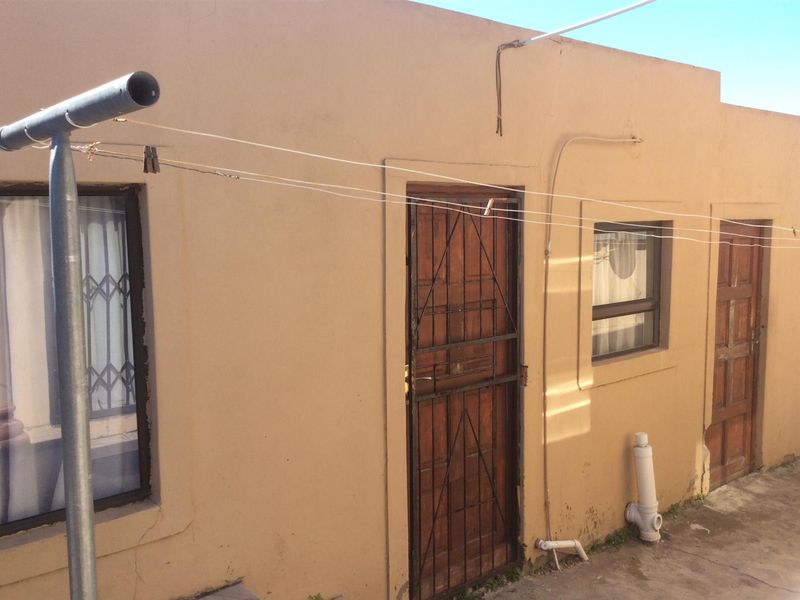 Rear exterior view of the property featuring a paved area, security gates, and wooden doors with visible wear on the exterior walls.