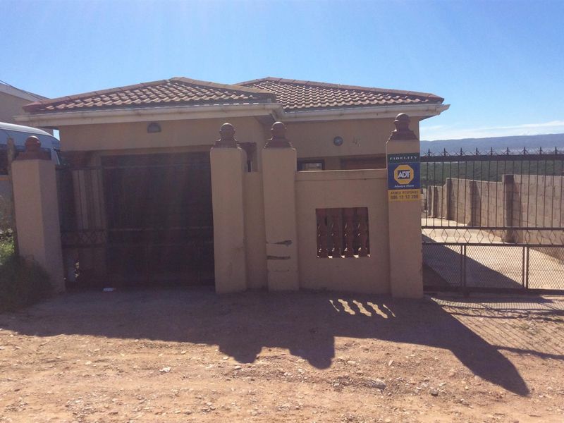 Front exterior view of a single-story house featuring a tiled roof, perimeter wall, and metal security gate.