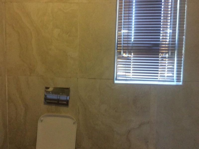 A functional bathroom featuring tiled walls, a wall-mounted toilet with a recessed flush plate, and a bathtub with a window.
