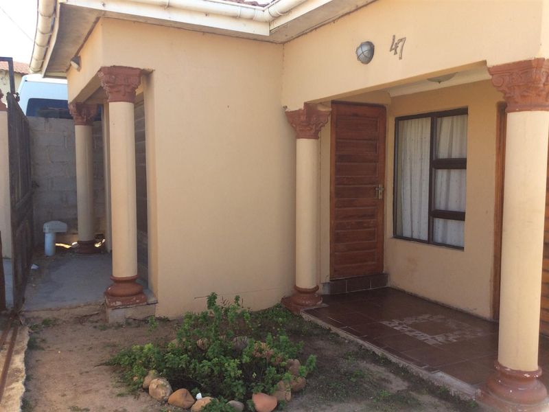 Front entrance area featuring a covered porch with decorative columns, a wooden door, and tiled flooring, showing signs of exterior wear.