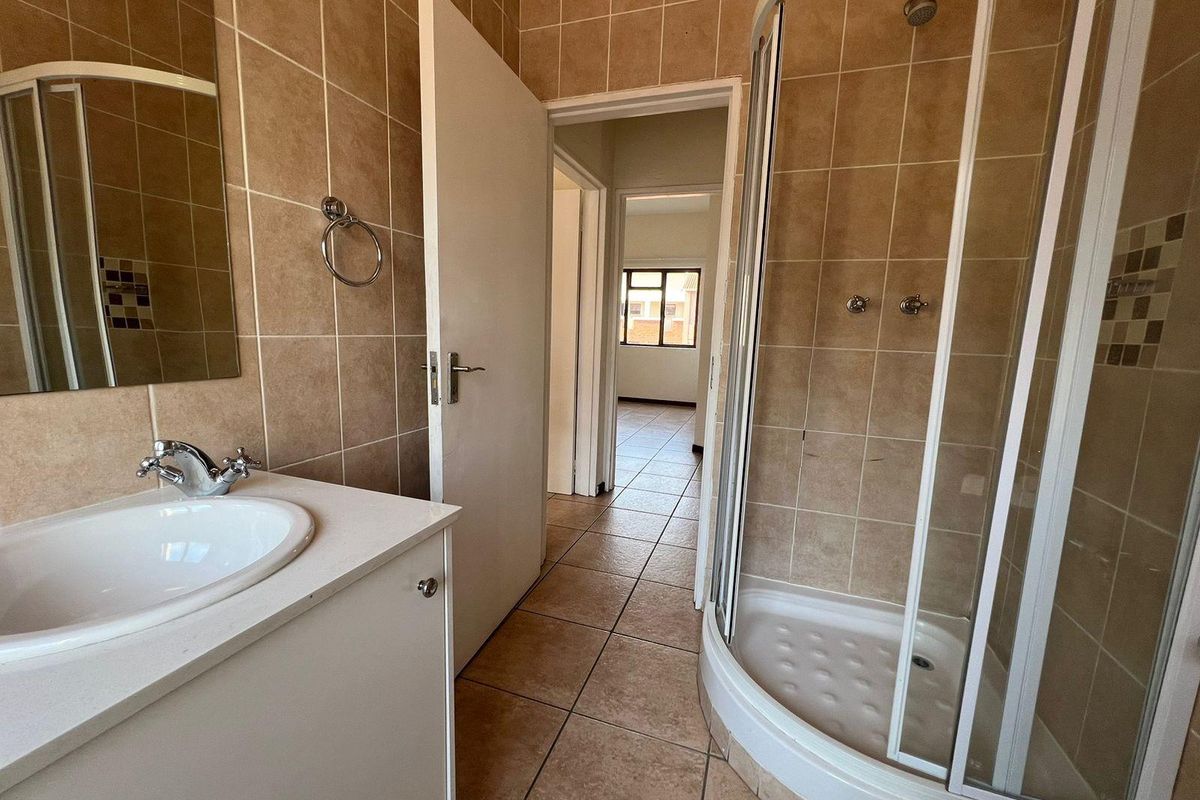 A functional bathroom featuring a corner shower enclosure, vanity cabinet with basin, and neutral tiled finishes throughout.
