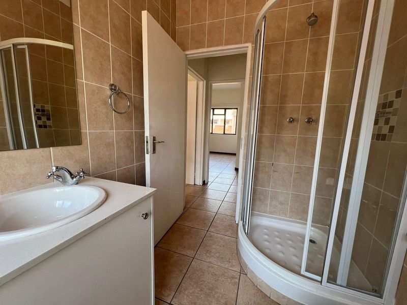 A functional bathroom featuring a corner shower enclosure, vanity cabinet with basin, and neutral tiled finishes throughout.