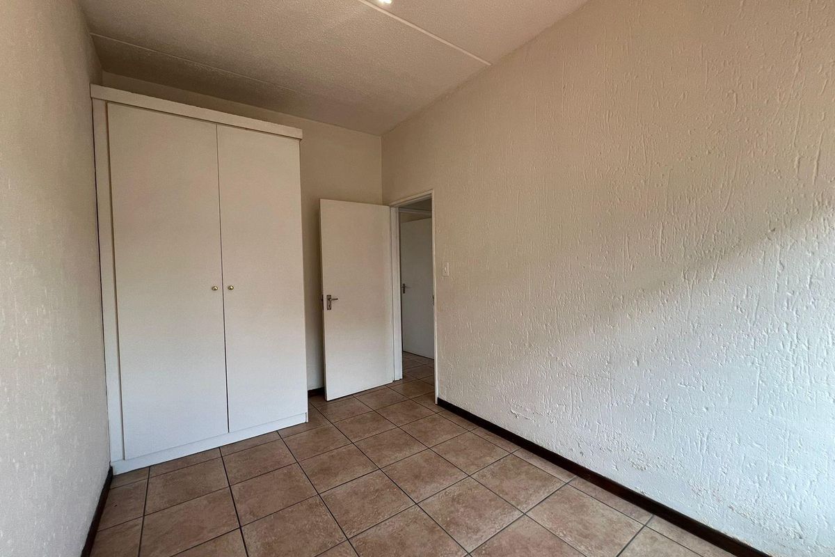 An empty bedroom featuring tiled flooring, textured walls, and a built-in wardrobe, offering a blank canvas for potential updates.