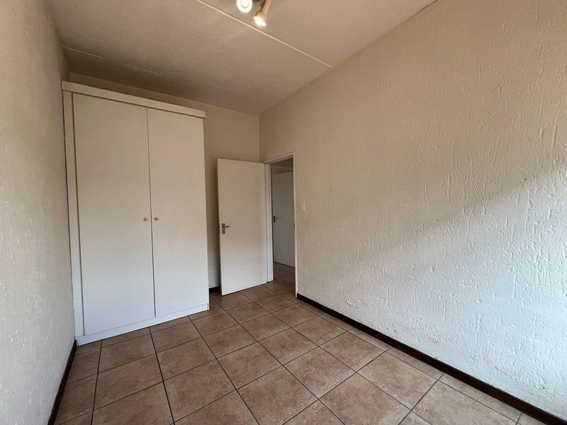 An empty bedroom featuring tiled flooring, textured walls, and a built-in wardrobe, offering a blank canvas for potential updates.