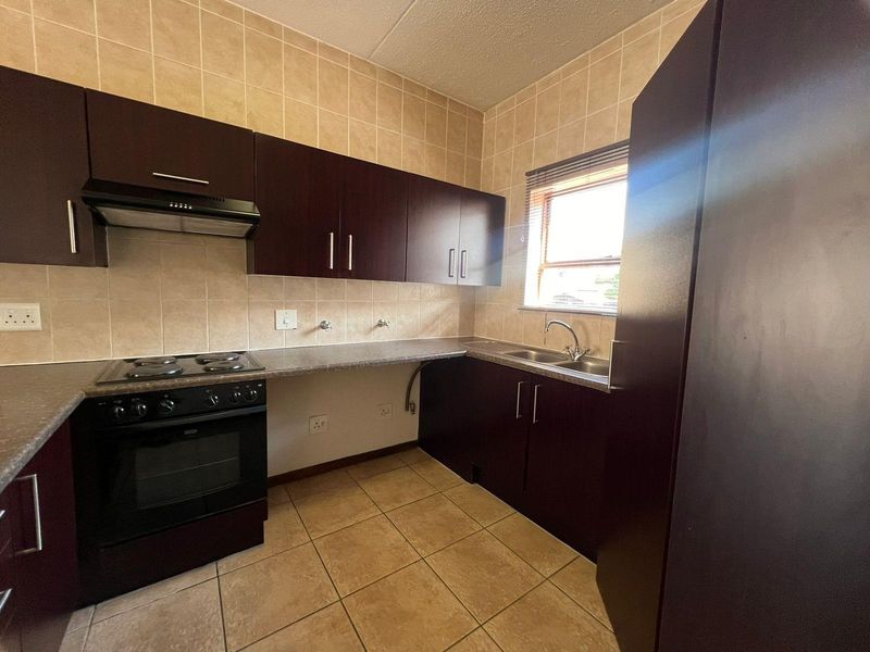 A functional kitchen featuring dark wood cabinetry, laminate countertops, a built-in oven with hob, and tiled finishes throughout.