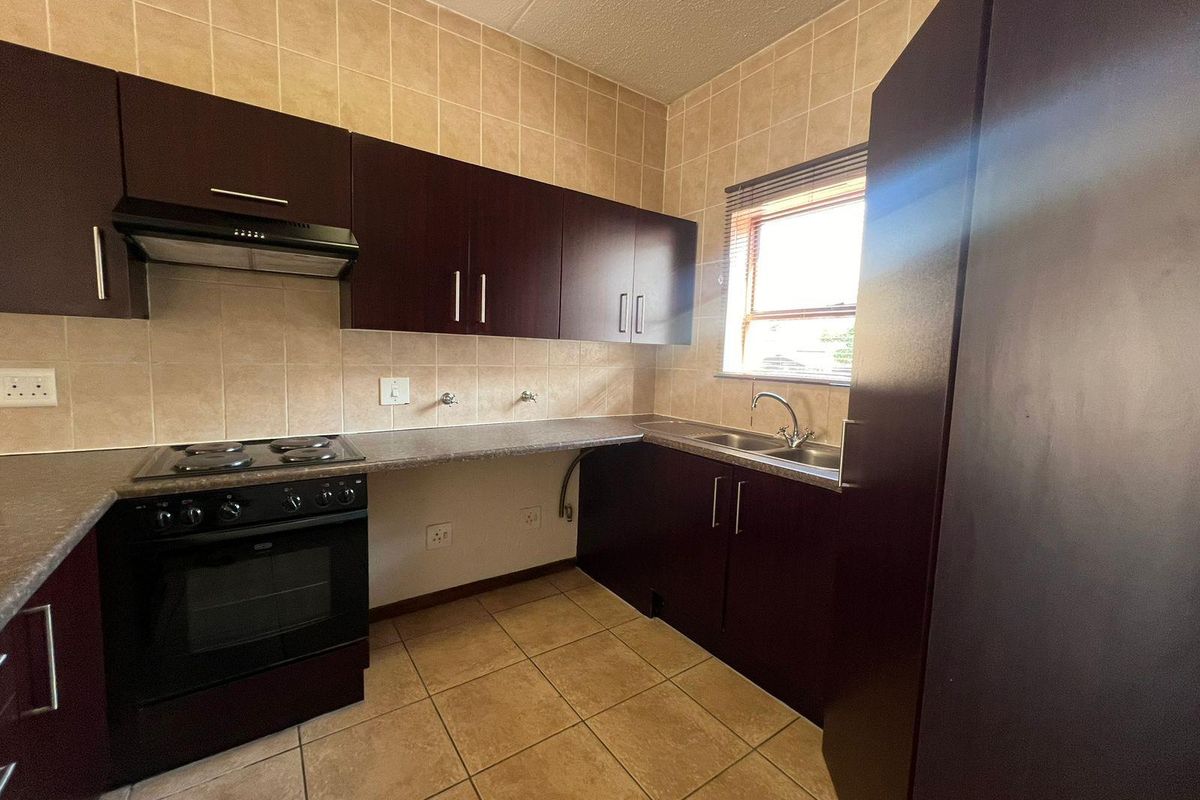 A functional kitchen featuring dark wood cabinetry, laminate countertops, a built-in oven with hob, and tiled finishes throughout.