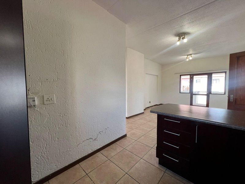 An open-plan living and kitchen area featuring tiled flooring, a dark wood kitchen island, and textured wall finishes with visible plaster cracking.