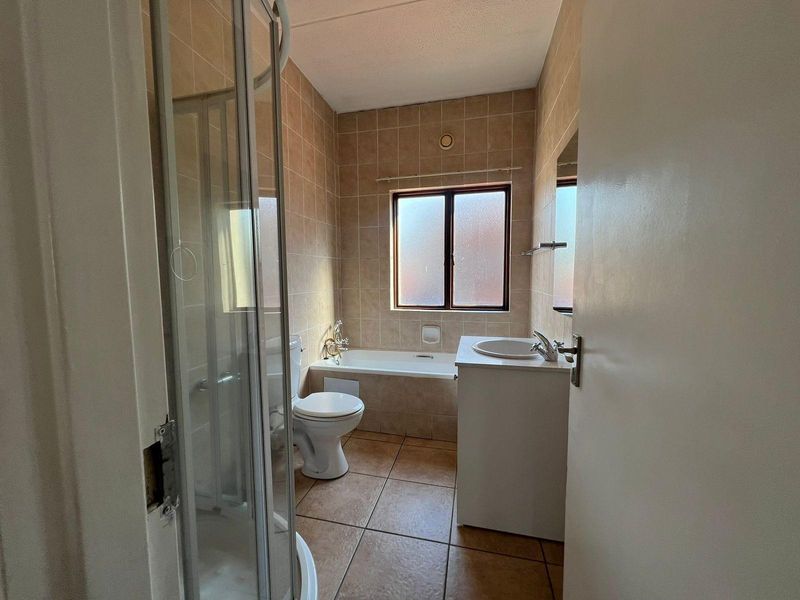 A functional bathroom featuring a shower enclosure, bathtub, toilet, and vanity basin with neutral tiled finishes throughout.