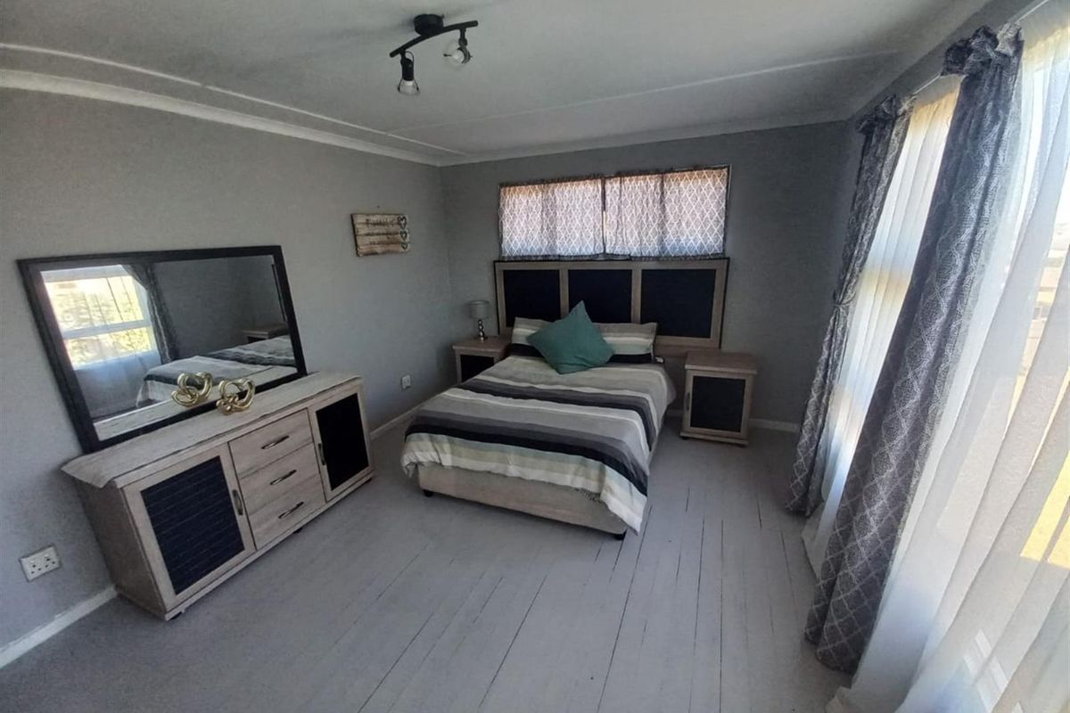 A well-lit bedroom featuring painted timber flooring, neutral wall tones, and large windows allowing for ample natural light.