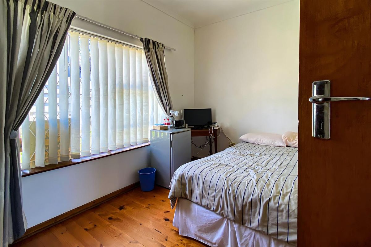 A bedroom featuring polished timber flooring, vertical blinds, and a standard door entrance.