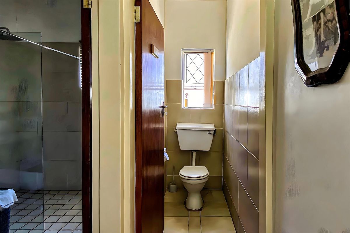 A compact bathroom featuring a standard toilet, tiled walls, and a small window, with an adjacent shower area visible through the doorway.