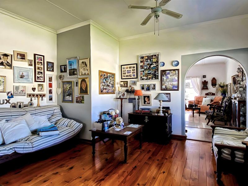 A cozy living room featuring polished timber flooring, a ceiling fan, and an arched doorway leading to an adjacent living space.