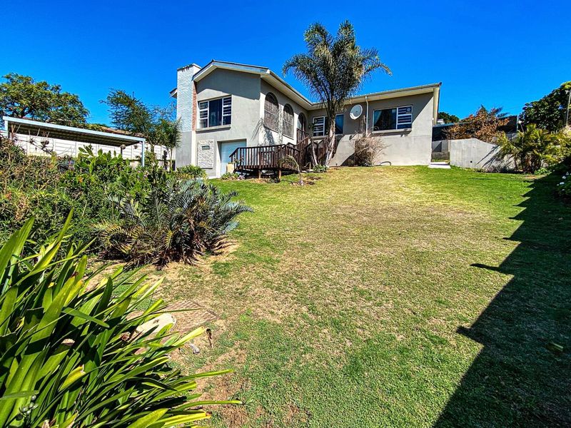 Rear view of the house featuring a spacious lawn, established garden, and an elevated wooden deck attached to the main structure.