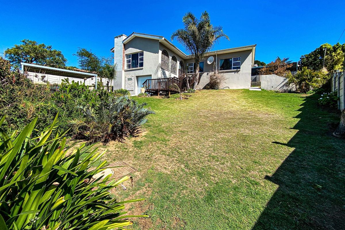 Rear view of the house featuring a spacious lawn, established garden, and an elevated wooden deck attached to the main structure.