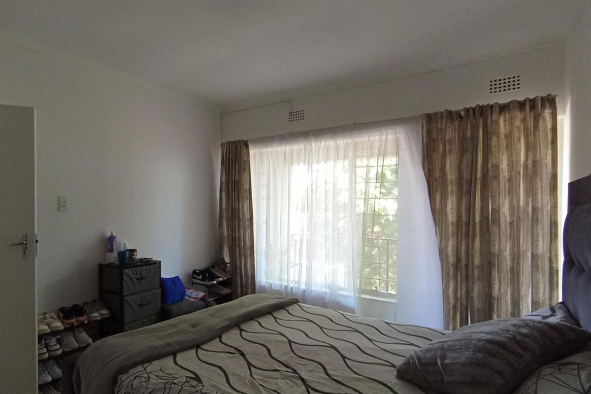 A bedroom featuring a large window with curtains and built-in ventilation grilles, providing natural light and access to an outdoor balcony area.