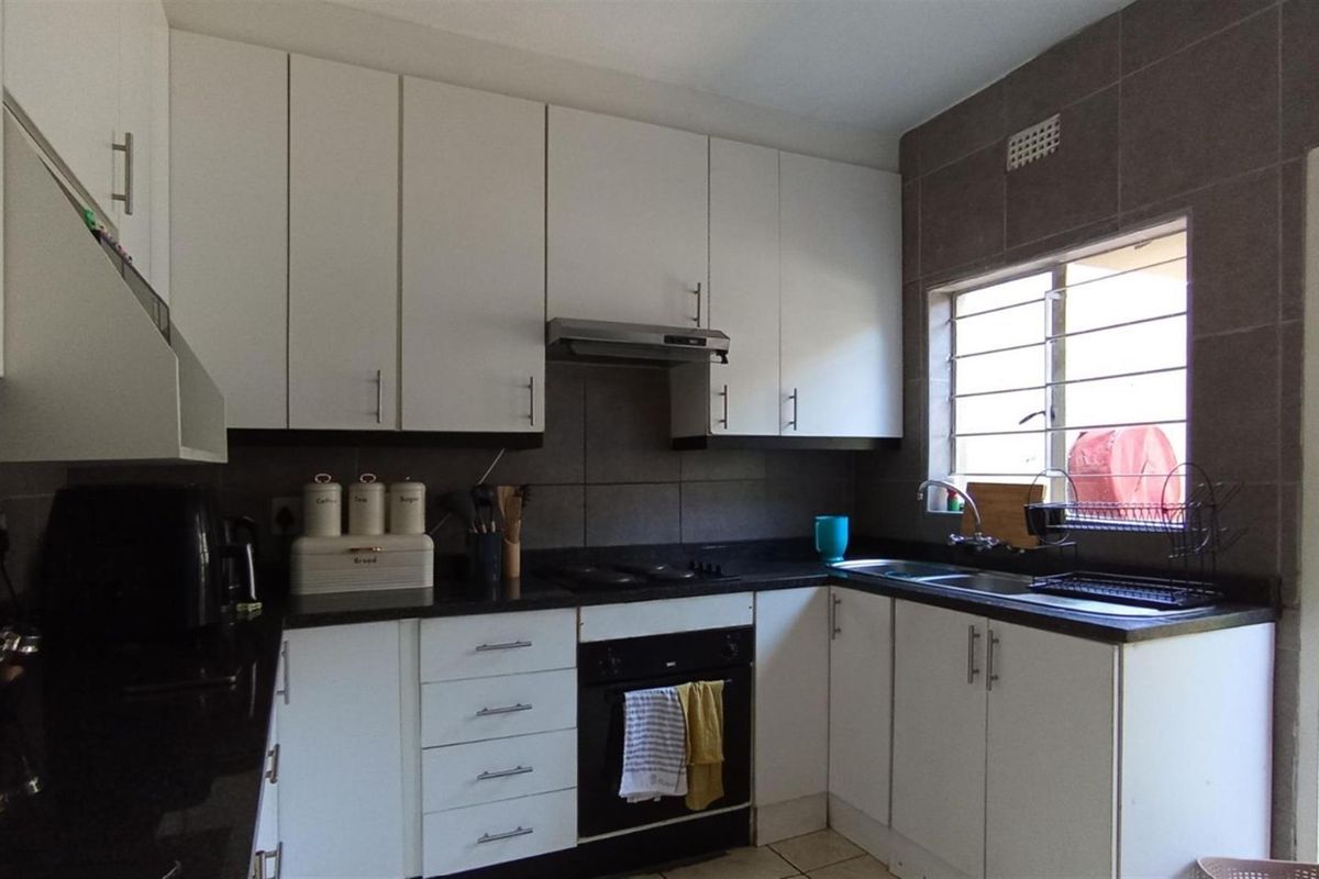 A functional kitchen featuring white cabinetry, dark stone countertops, a built-in oven, extractor fan, and a double sink with a window view.