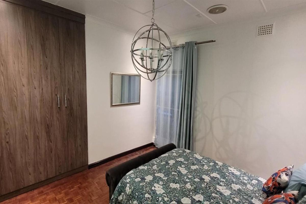 A well-maintained bedroom featuring polished parquet flooring, built-in wooden cupboards, and a decorative pendant light fixture.