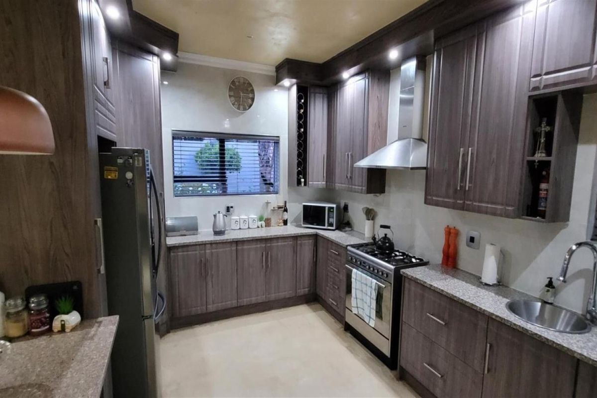 Modern kitchen featuring dark wood cabinetry, granite countertops, stainless steel extractor fan, and a gas stove.
