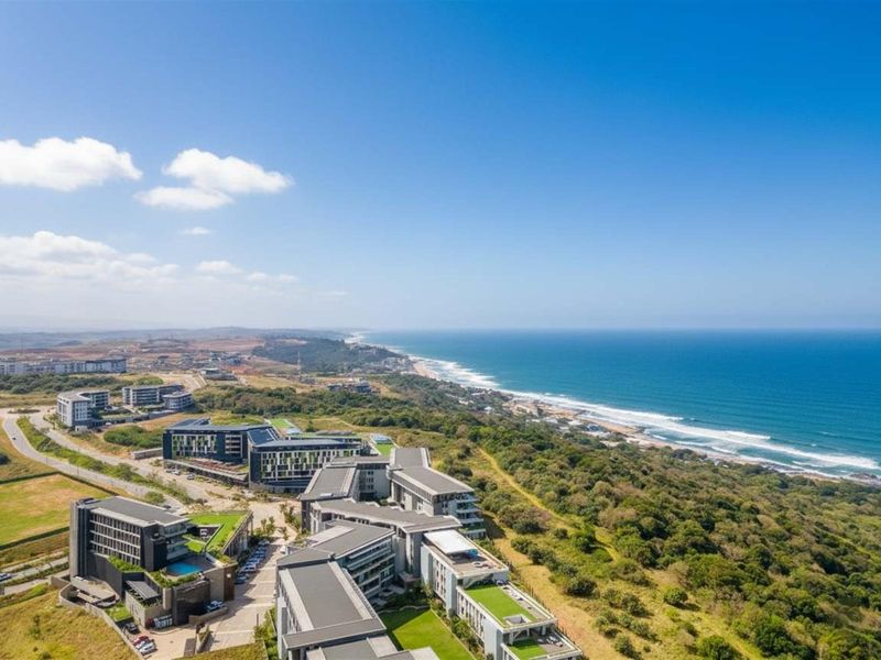 An aerial view of a modern residential apartment complex situated along the coastline, featuring green roofs and proximity to the ocean.
