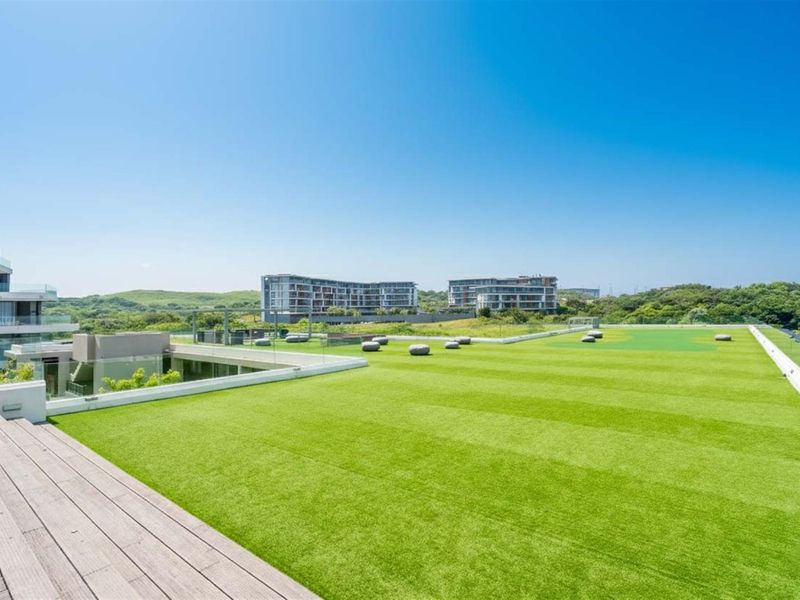 Expansive rooftop terrace featuring timber decking, artificial turf, and a modern glass balustrade with panoramic views of the surrounding estate.
