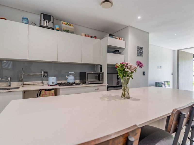 Modern kitchen featuring sleek white cabinetry, stone countertops, a gas hob, and a glass splashback, seamlessly integrated into an open-plan living space.