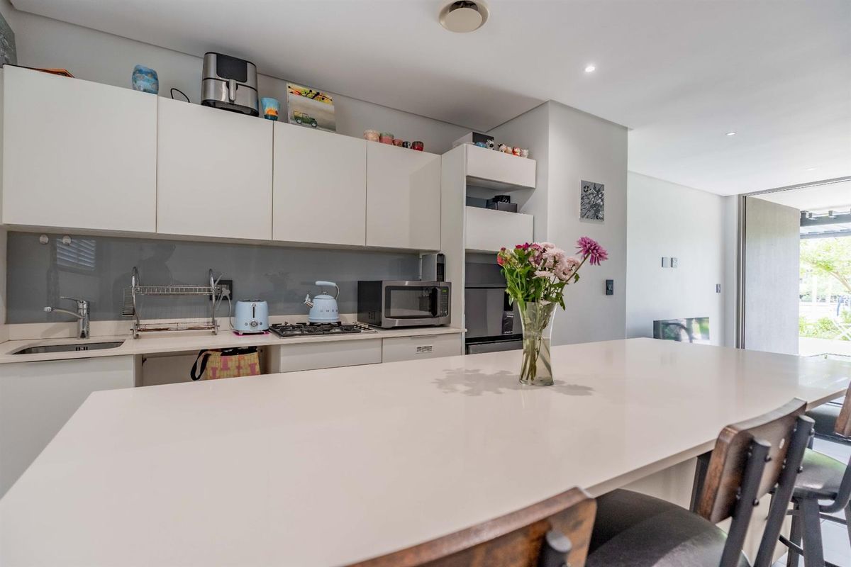 Modern kitchen featuring sleek white cabinetry, stone countertops, a gas hob, and a glass splashback, seamlessly integrated into an open-plan living space.