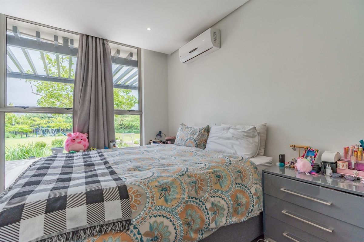 A bright bedroom featuring large floor-to-ceiling windows with garden views and a wall-mounted split-system air conditioner.