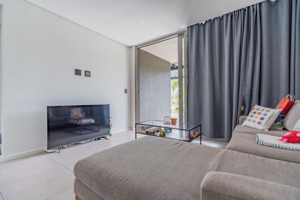 A bright living room featuring large sliding glass doors that open to an outdoor area, complemented by neutral tiled flooring and recessed lighting.